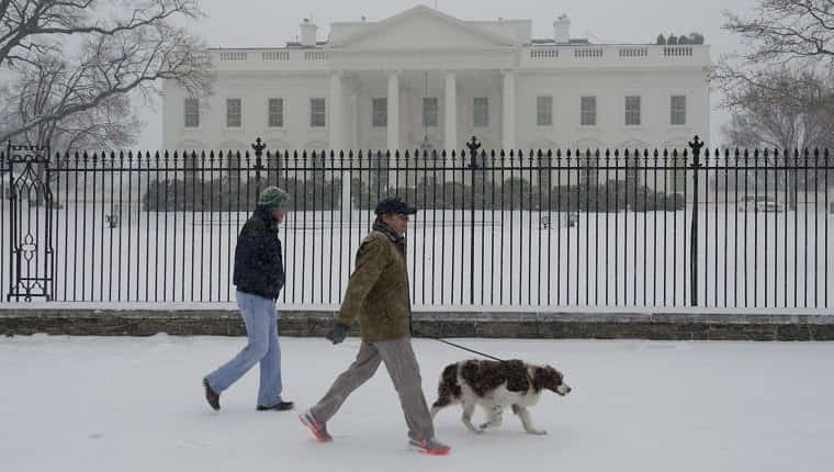 La gente paseaba a un perro durante una tormenta de nieve frente a la Casa Blanca en Washington, DC, el 3 de marzo de 2014. La nieve comenzó a caer en la capital del país el lunes, y las autoridades advirtieron a la gente que se mantuviera alejada de las carreteras heladas y traicioneras, un escenario que se ha vuelto familiar para los residentes del Medio Oeste, Este e incluso el Sur Profundo este año.  Las escuelas fueron canceladas, el servicio de autobús se interrumpió en algunos lugares y se ordenó a los funcionarios del gobierno federal en el área de DC que se quedaran en casa el lunes. 